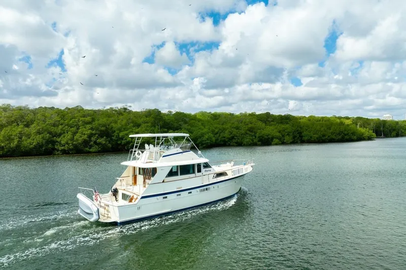 Dharma Yacht Photos Pics 1978 Hatteras 53 Yacht Fisherman cruising on a scenic river under a cloudy sky.