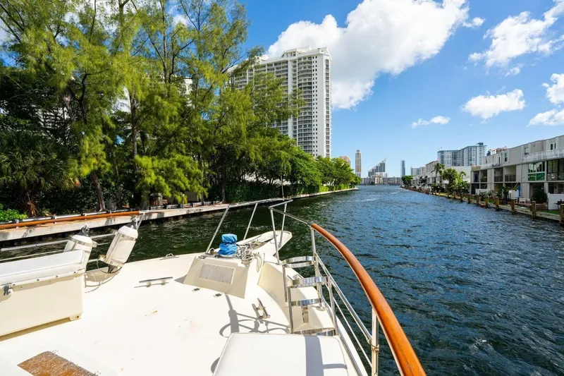 Dharma Yacht Photos Pics 1978 Hatteras 53 Yacht Fisherman cruising a scenic urban waterway with lush greenery.