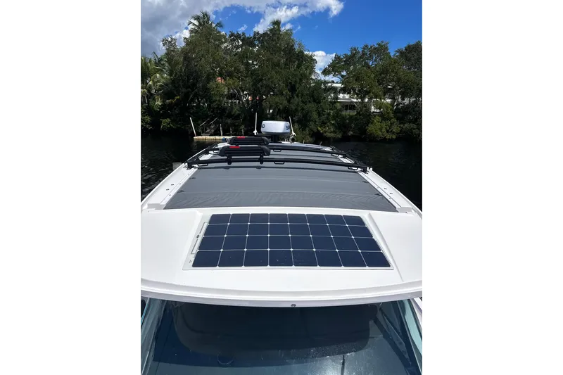 Axopar 37 Suntop Yacht Photos Pics 2024 Axopar 37 SunTop with solar panel, docked near lush greenery under a clear blue sky.