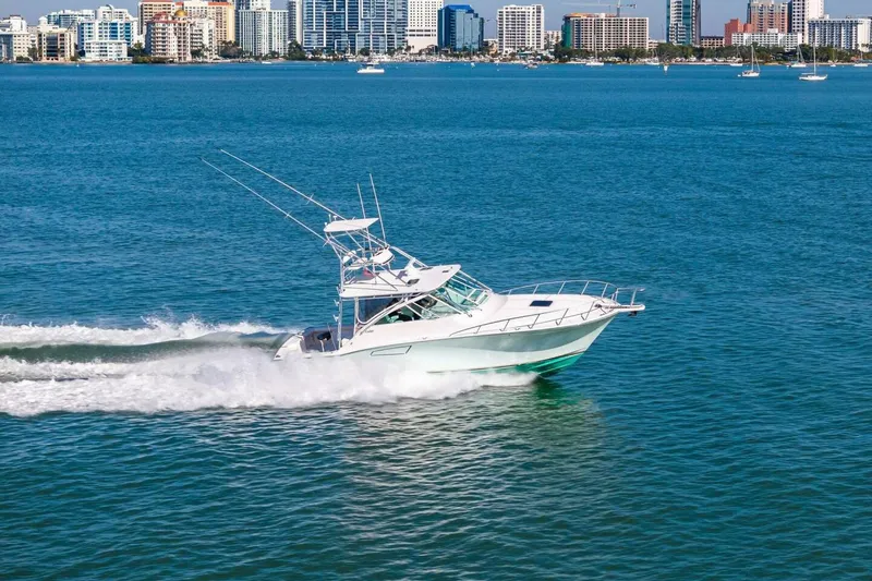 Miss B Havin Yacht Photos Pics 2005 Cabo 40 Express yacht cruising on blue water with city skyline backdrop.