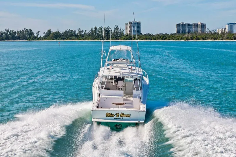 Miss B Havin Yacht Photos Pics 2005 Cabo 40 Express yacht cruising on clear blue waters near a coastal city.
