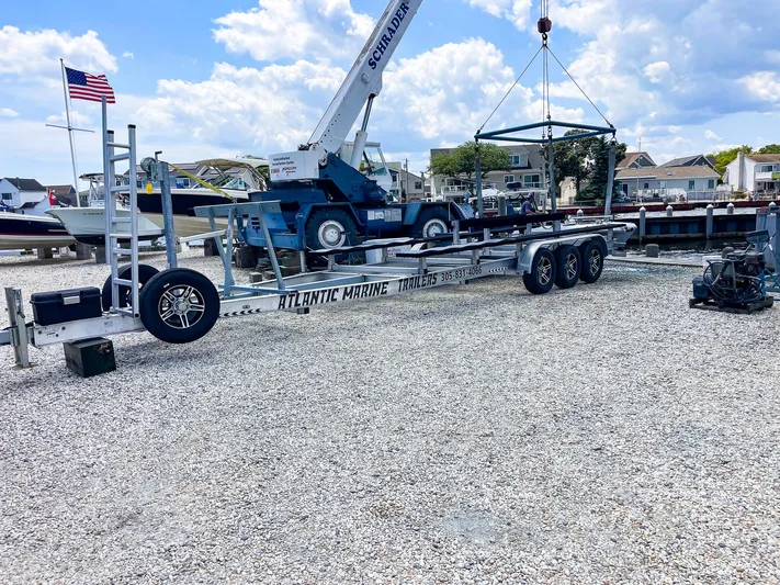  Yacht Photos Pics Boat trailer at marina with crane, gravel lot, and American flag in background.