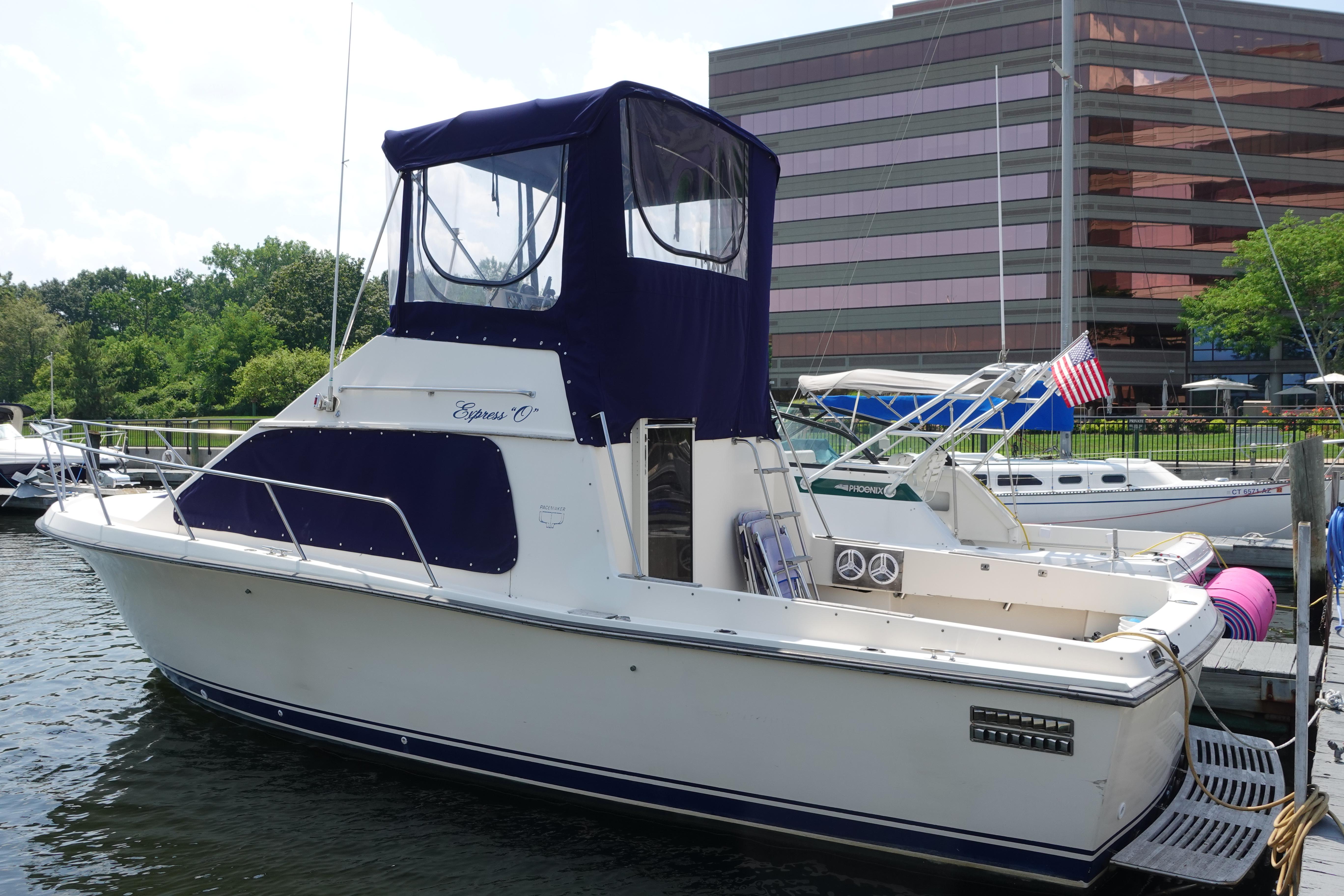 1988 Pacemaker 308 boat docked near modern building, featuring blue canopy and American flag.