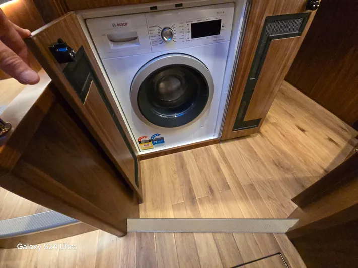 Ocean Driver Yacht Photos Pics Washing machine inside 2022 Riviera 54 Enclosed Flybridge, wooden cabinetry, and flooring.