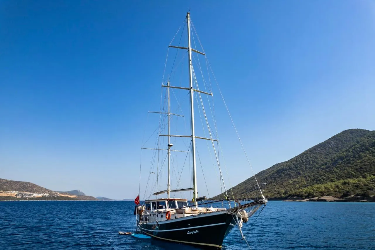 Sailing yacht on blue sea with mountainous background, clear sky, 1990 custom model.
