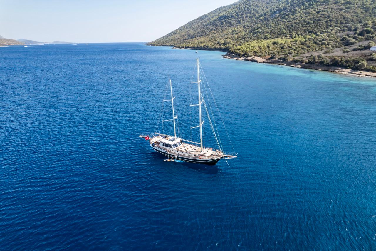 Sailing yacht on blue sea near forested coastline, custom model from 1990.