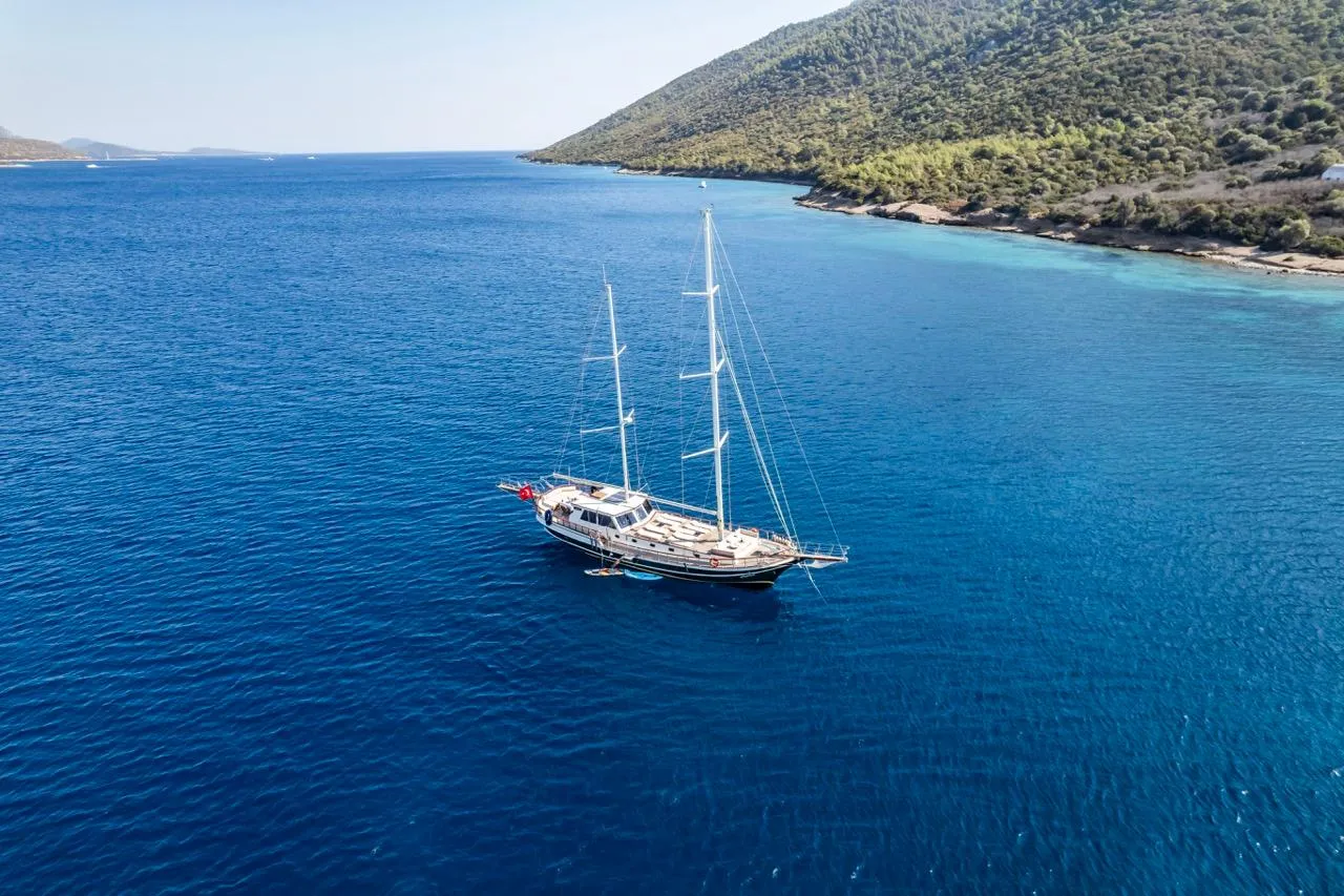 Sailing yacht on blue sea near forested coastline, custom model from 1990.