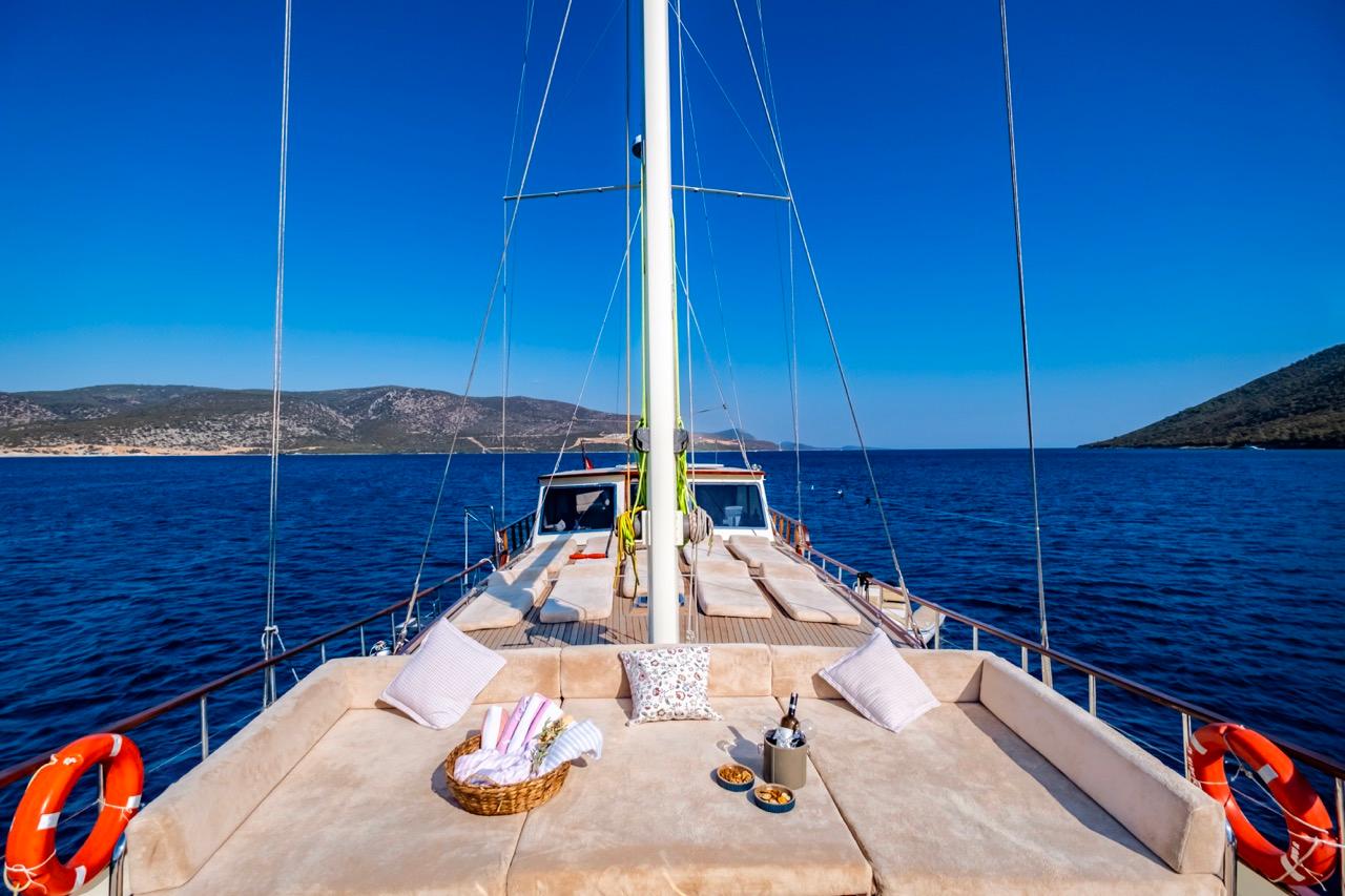 Luxurious yacht deck with cushions, basket, and drinks, sailing on a serene blue sea.