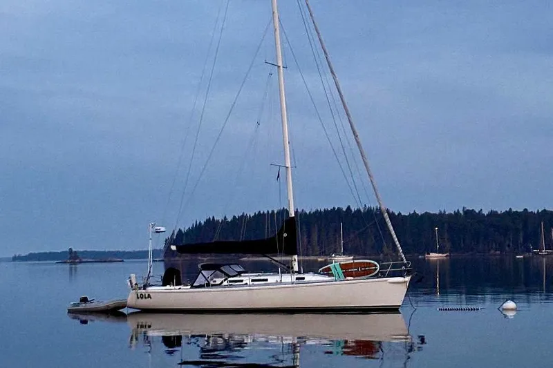 Lola Yacht Photos Pics Sailboat J/130 from 1995 by J Boats, anchored on calm water with forest backdrop.