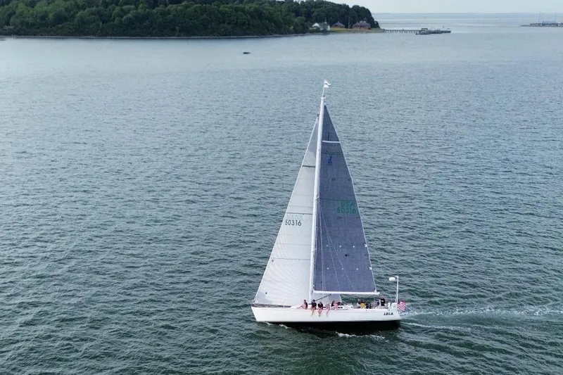 Lola Yacht Photos Pics Sailboat J/130 from 1995 cruising on open water near a forested shoreline.