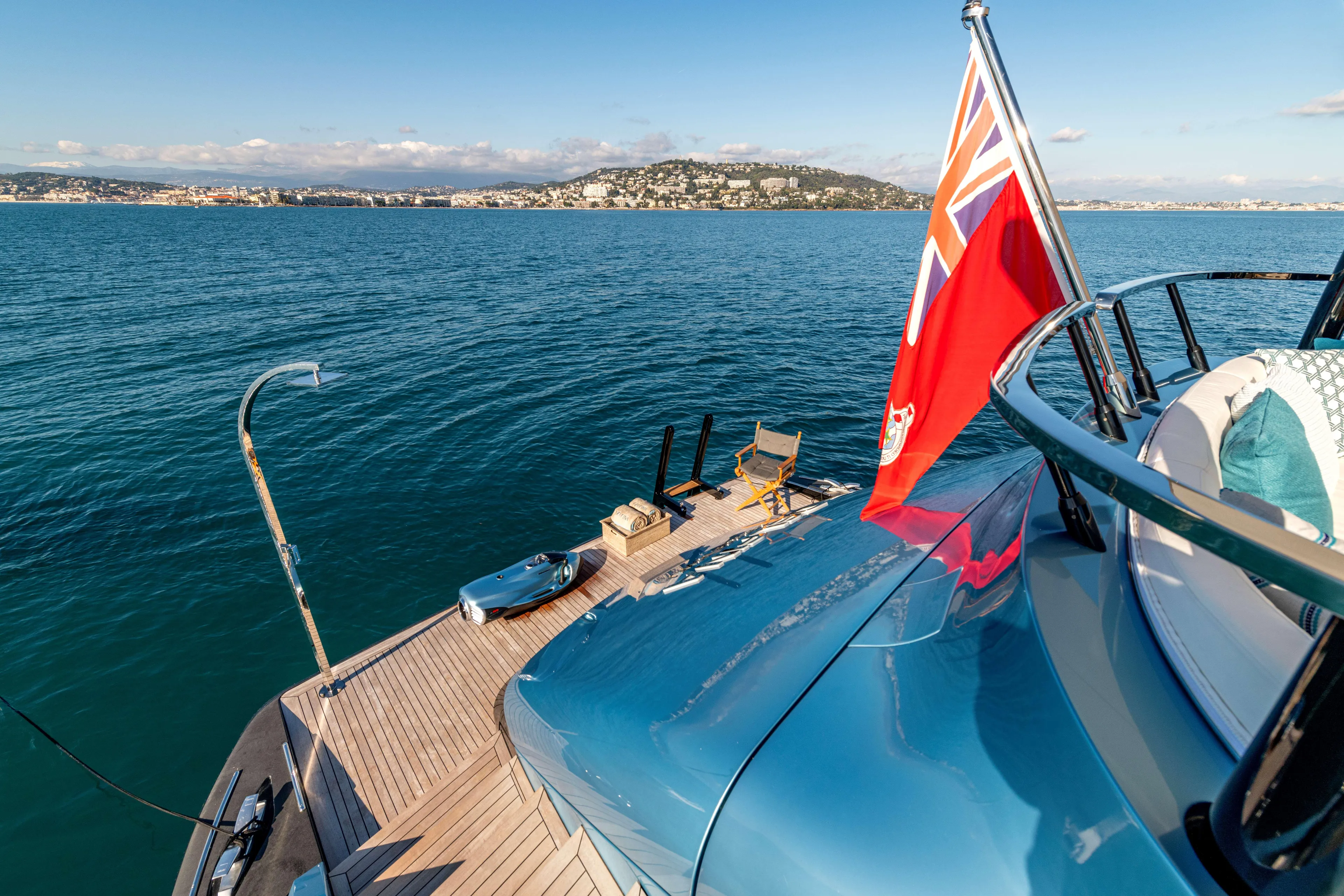 Delfina Yacht Photos Pics 2024 Mangusta 104 REV yacht with flag, overlooking serene ocean and distant coastline.