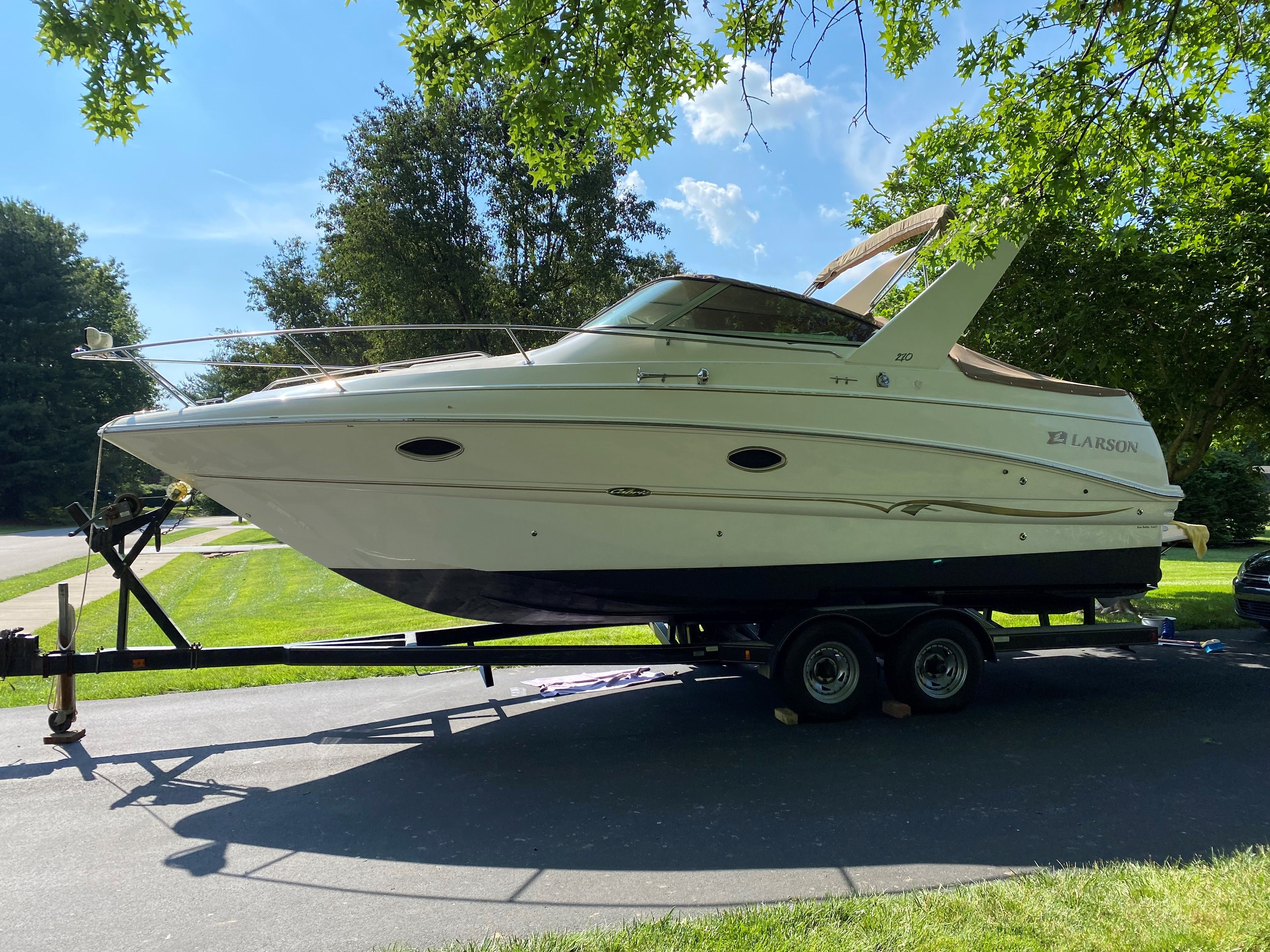 2001 Larson Cabrio 270 boat on trailer, parked outdoors under trees.
