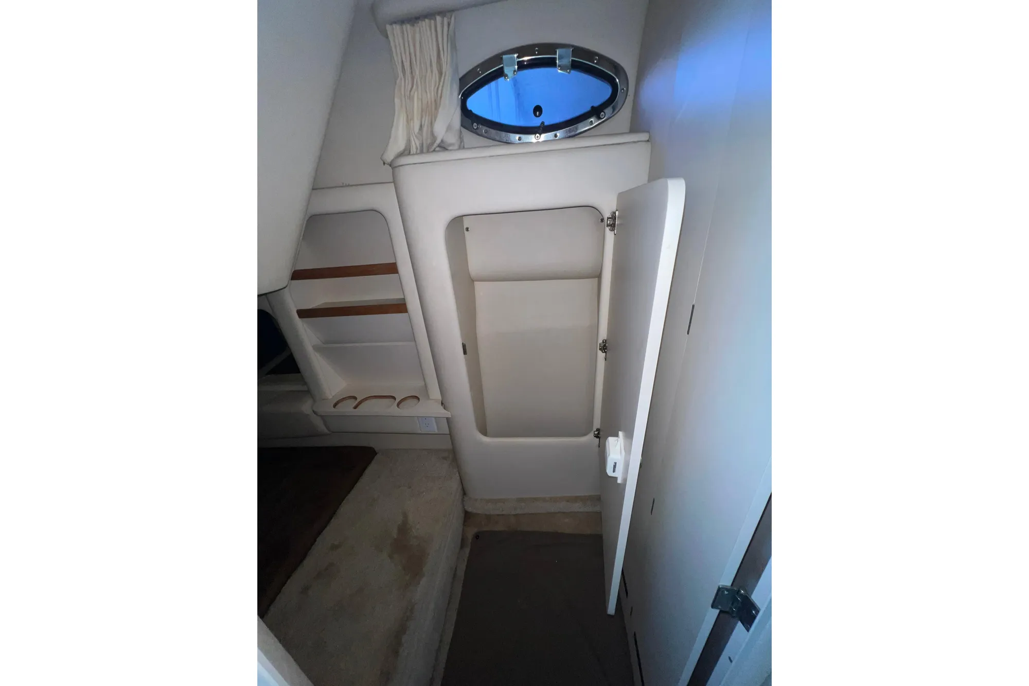 1999 Sea Ray 290 Sundancer cabin interior with open storage compartment and porthole window.