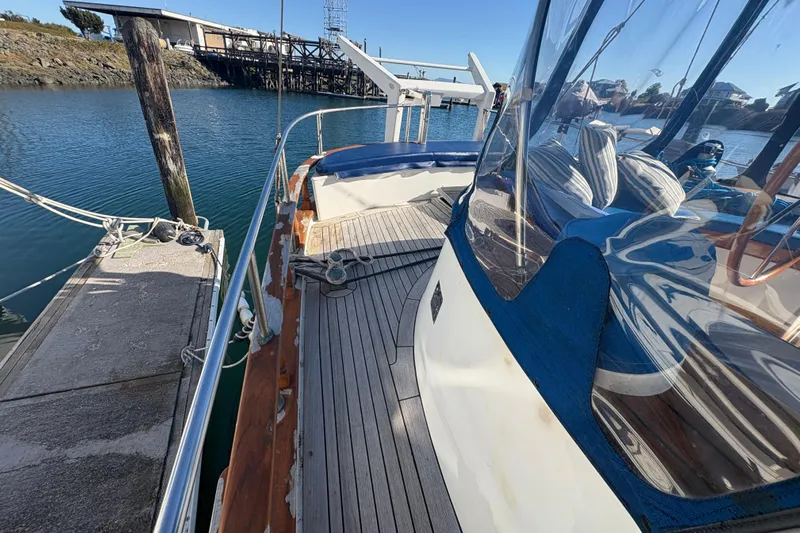 Tenacious Yacht Photos Pics 1987 Mikelson 50 yacht docked, featuring wooden deck and blue canopy, in a serene marina setting.