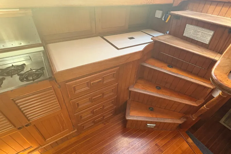 Tenacious Yacht Photos Pics 1987 Mikelson 50 yacht interior with wooden cabinetry and stairs, featuring a compact kitchen area.