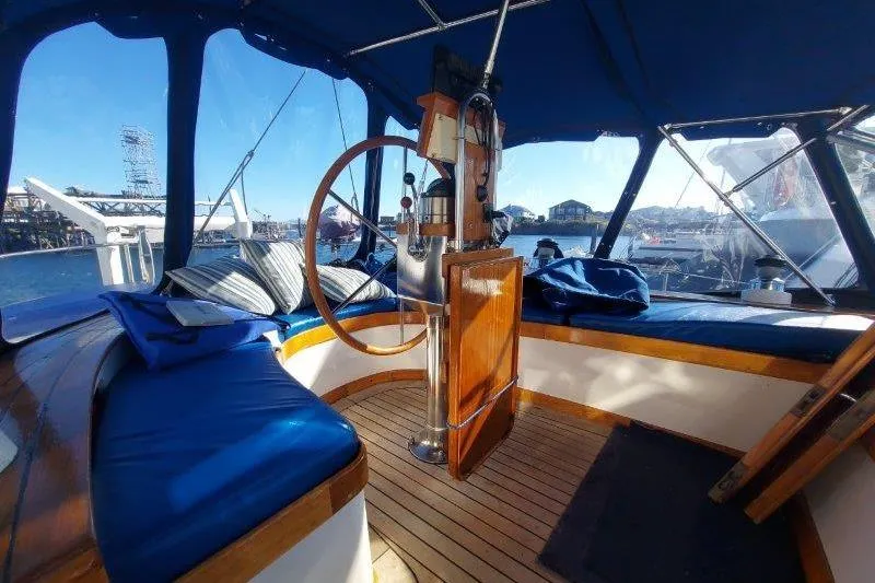Tenacious Yacht Photos Pics Interior view of 1987 Mikelson 50 yacht with wooden steering wheel and blue seating.