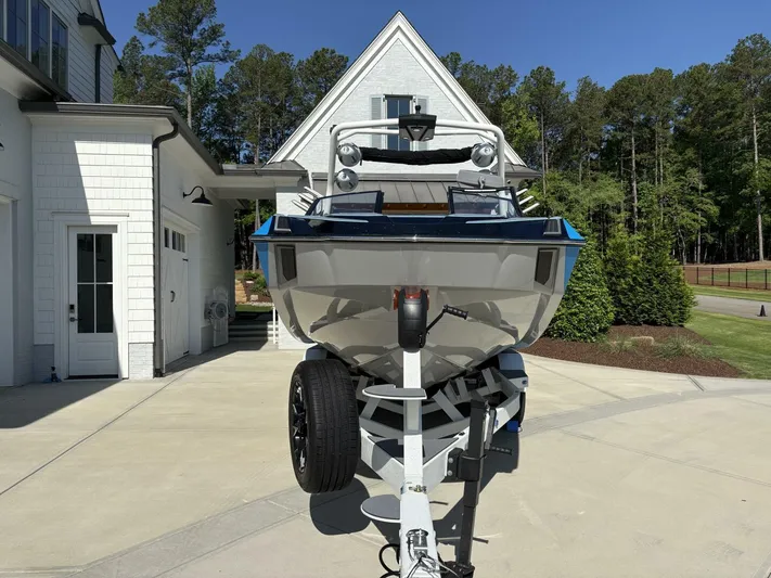  Yacht Photos Pics 2024 Malibu M242 boat on trailer in driveway, surrounded by trees and house.