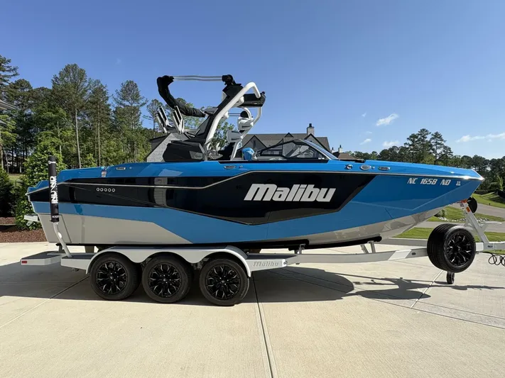 Yacht Photos Pics 2024 Malibu M242 boat on trailer, blue and black design, parked outdoors.