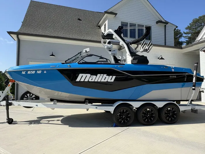  Yacht Photos Pics 2024 Malibu M242 boat in blue and black on a trailer, parked outside a house.