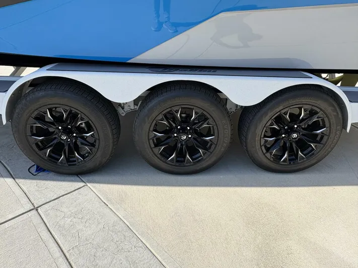  Yacht Photos Pics 2024 Malibu M242 boat trailer with three black wheels on a concrete surface.