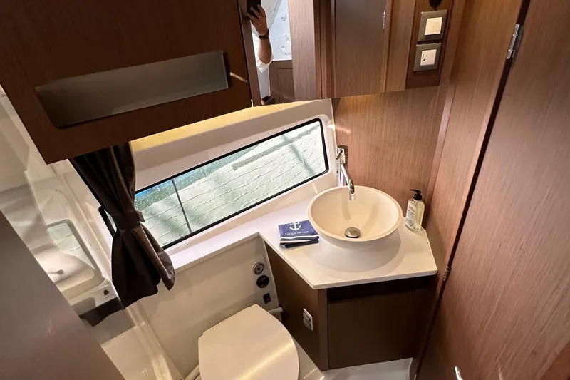 Vitamin Sea Yacht Photos Pics 2023 Beneteau Antares 11 Fly bathroom with modern sink, window, and wooden cabinetry.