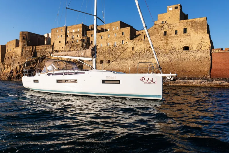 Ssy 01 Yacht Photos Pics 2021 Jeanneau Sun Odyssey 440 sailing near historic stone buildings on a sunny day.