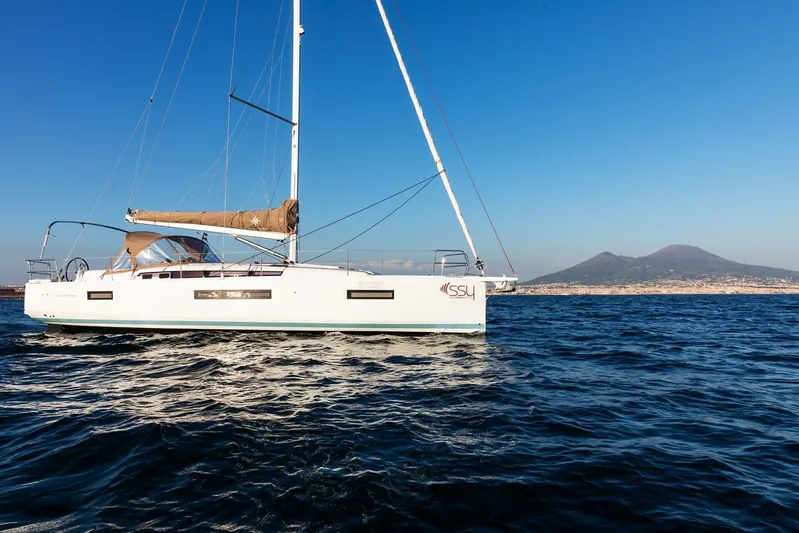 Ssy 01 Yacht Photos Pics 2021 Jeanneau Sun Odyssey 440 sailing near a coastal mountain under clear blue skies.