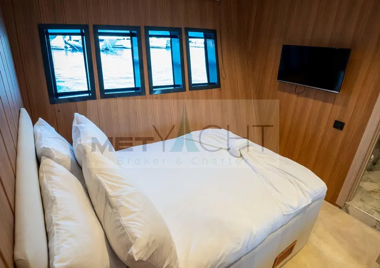  Yacht Photos Pics Luxurious 2024 custom trawler bedroom with wood paneling, windows, and wall-mounted TV.