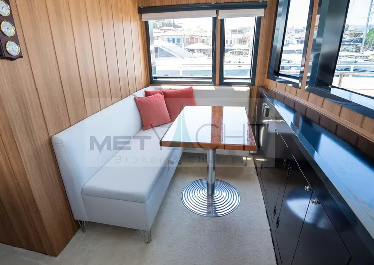 Yacht Photos Pics Interior of 2024 Custom Trawler with white seating, wooden table, and large windows.