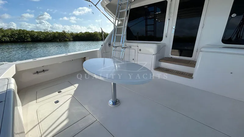 Sin Plan Yacht Photos Pics Bertram 630E 2005 yacht deck with table and ladder, docked by the water.