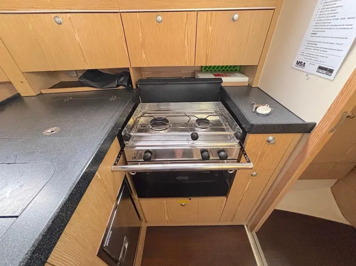 Sunshine Yacht Photos Pics Compact kitchen in a 2014 Hanse 345 yacht with stove, oven, and wooden cabinetry.