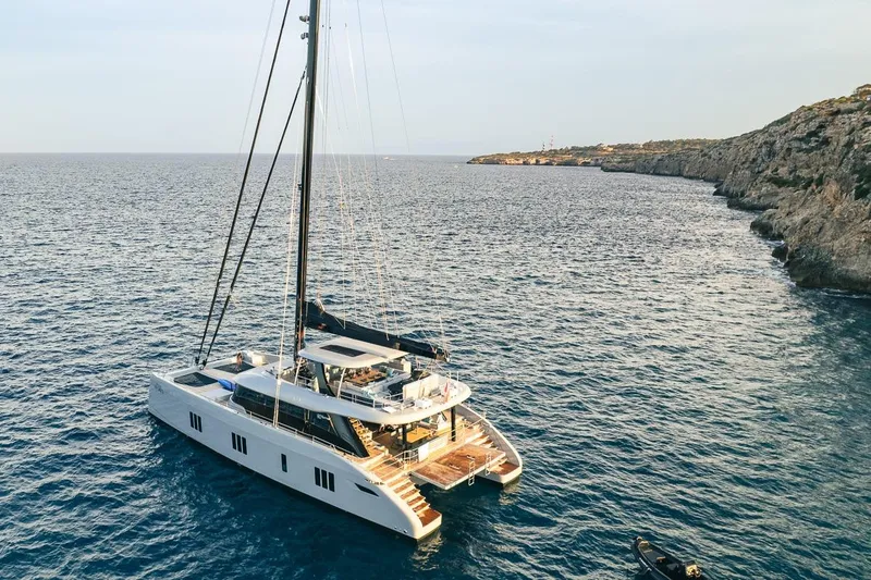 Shades Of Grey Yacht Photos Pics 2024 Sunreef 80 sailing yacht anchored near rocky coastline.