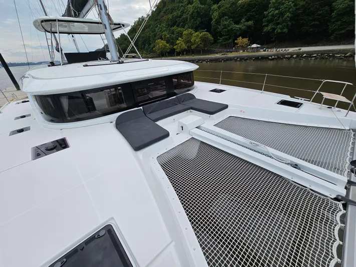  Yacht Photos Pics 2024 Lagoon 46 catamaran with spacious deck and seating, docked by a lush shoreline.