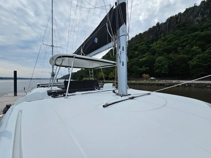  Yacht Photos Pics 2024 Lagoon 46 catamaran docked by lush green cliffs under a cloudy sky.