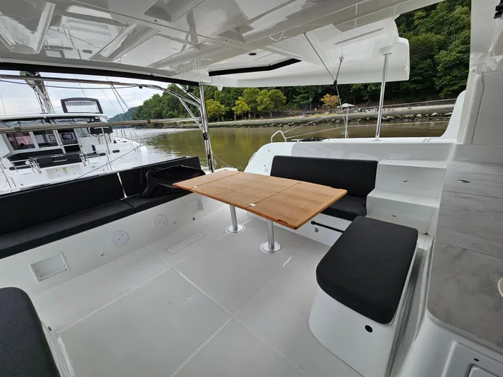  Yacht Photos Pics 2024 Lagoon 46 yacht cockpit with sleek seating and wooden table, docked by a serene river.