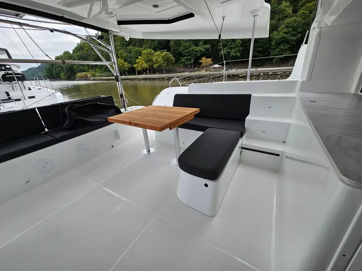  Yacht Photos Pics 2024 Lagoon 46 yacht deck with seating and table, surrounded by lush greenery.