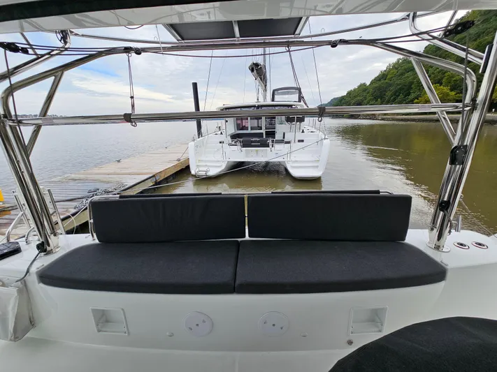  Yacht Photos Pics 2024 Lagoon 46 catamaran docked by a serene waterfront with lush greenery.