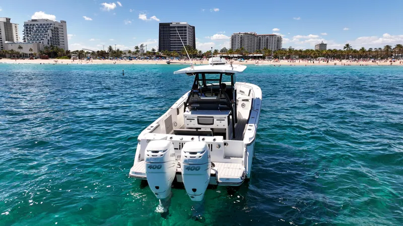  Yacht Photos Pics 2020 Blackfin 332 CC boat on clear blue water near a beach with buildings.
