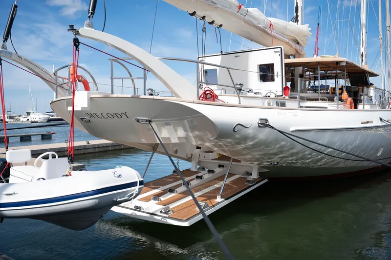 Melody Yacht Photos Pics 2022 Ridas Custom Yacht docked with tender boat, elegant design, sunny marina setting.