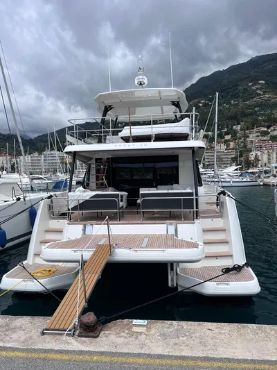  Yacht Photos Pics 2024 Beneteau M 48 yacht docked in marina, overcast sky, mountainous backdrop.