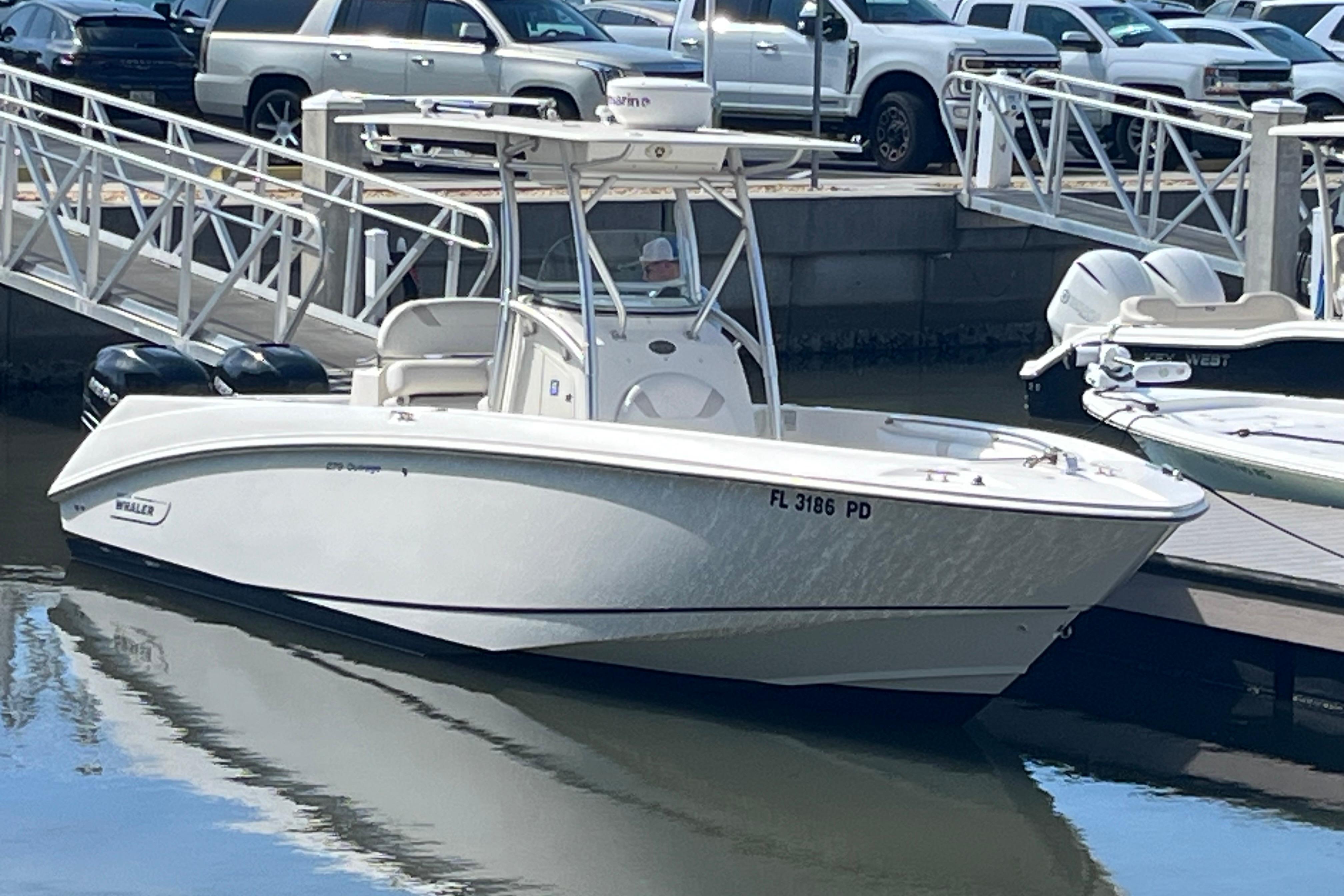 2007 Boston Whaler 270 Outrage boat docked at marina with vehicles in background.