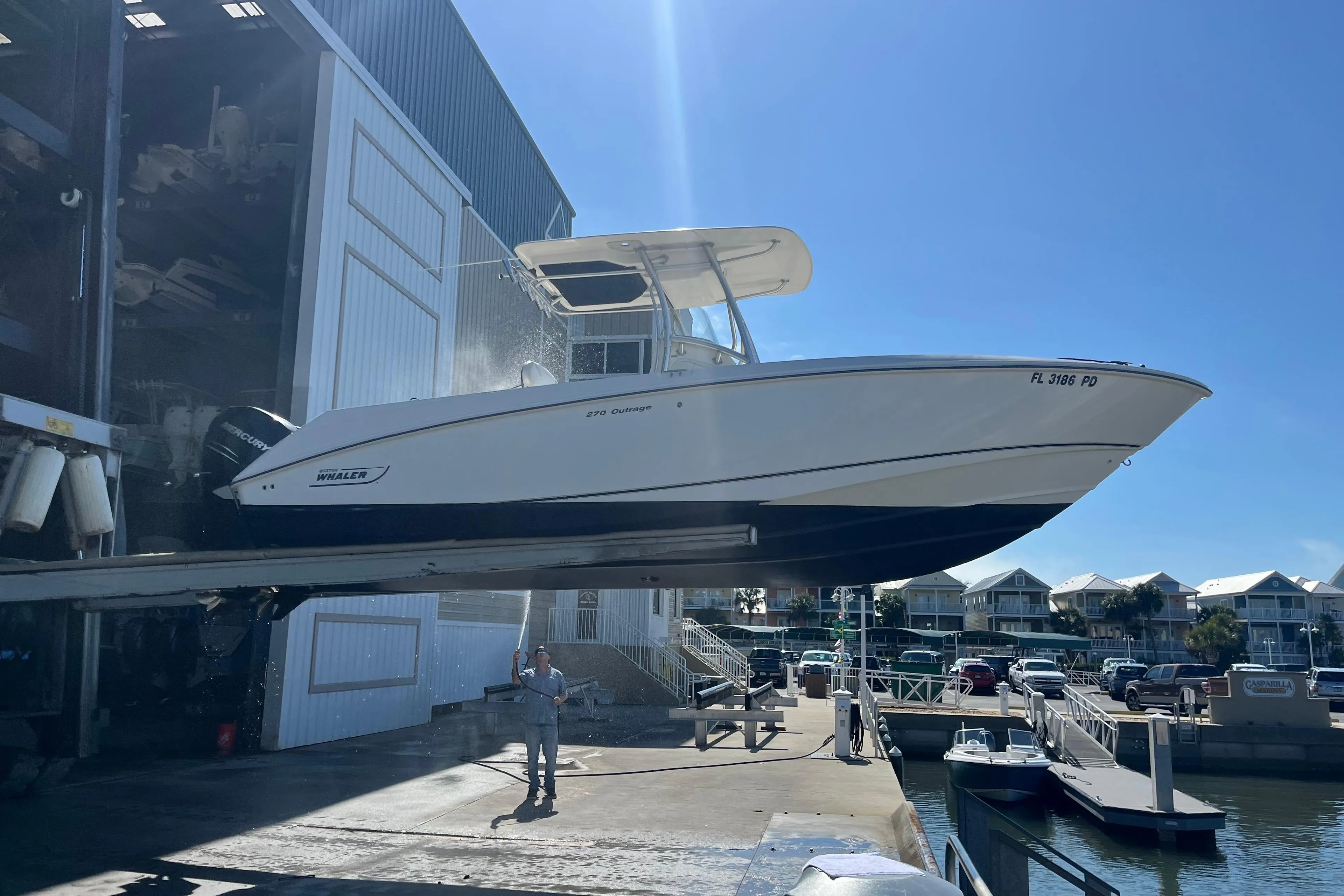 2007 Boston Whaler 270 Outrage being lifted at a marina under clear blue skies.