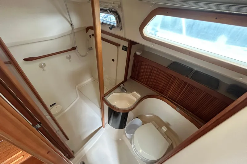 Indigo Yacht Photos Pics 2002 Sabre 362 yacht bathroom with shower, sink, and toilet, featuring wooden accents and window.