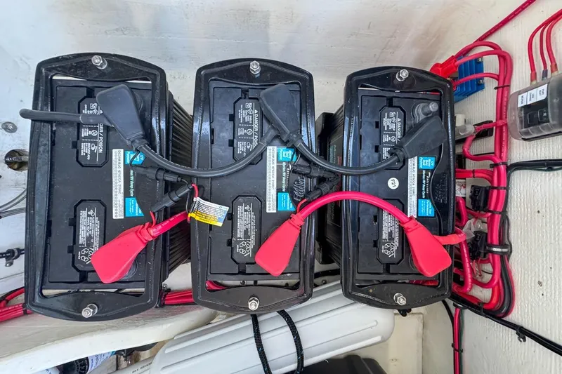  Yacht Photos Pics Three marine batteries in a 2022 Velocity 290sc boat, connected with red and black cables.