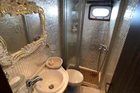 Luxurious yacht bathroom with ornate mirror, compact shower, and elegant fixtures.