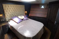 Luxurious yacht bedroom with tufted headboard, wooden accents, and cozy bedding. Custom 23m Epoxy Hull, 1991.
