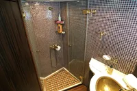 Luxurious yacht bathroom with mosaic tiles, glass shower, and brass sink fixtures.