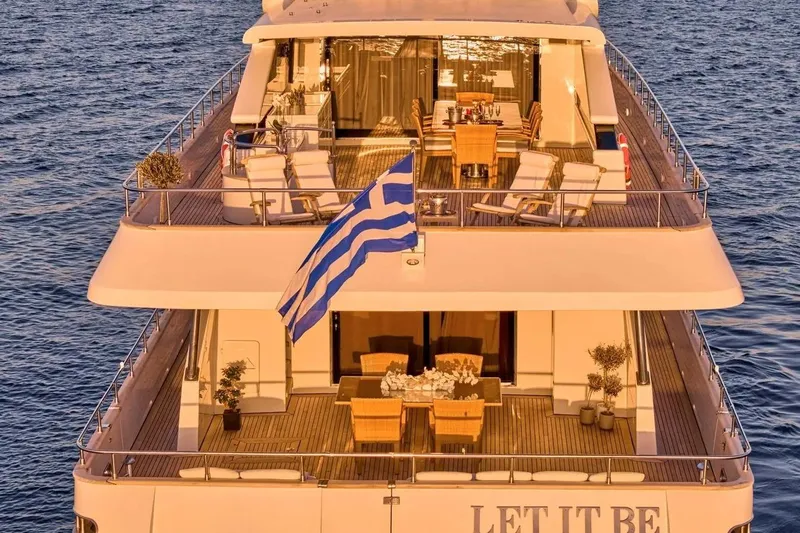 Let It Be Yacht Photos Pics Luxurious 1998 Tecnomarine Custom yacht with Greek flag, elegant deck, and dining area at sunset.