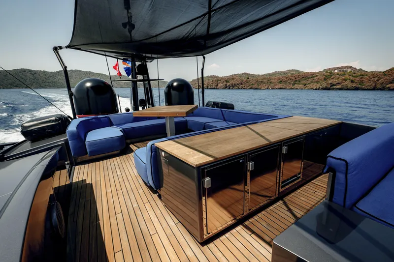 Ginger Yacht Photos Pics Luxurious 2006 Pershing 115 yacht deck with blue seating and wooden table, cruising near scenic coastline.