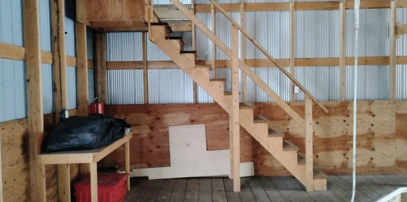  Yacht Photos Pics Wooden staircase and workbench inside a custom boathouse, featuring corrugated metal walls.
